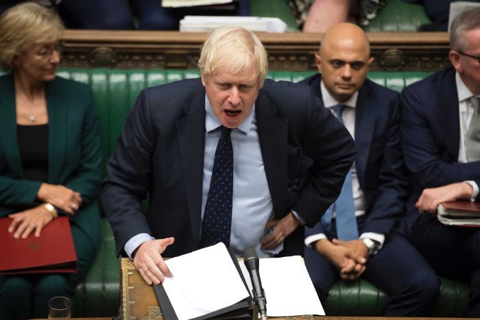 Boris Johnson stands at the lectern to speak in the House of Commons. He is mid-speech and wears a serious expression. 