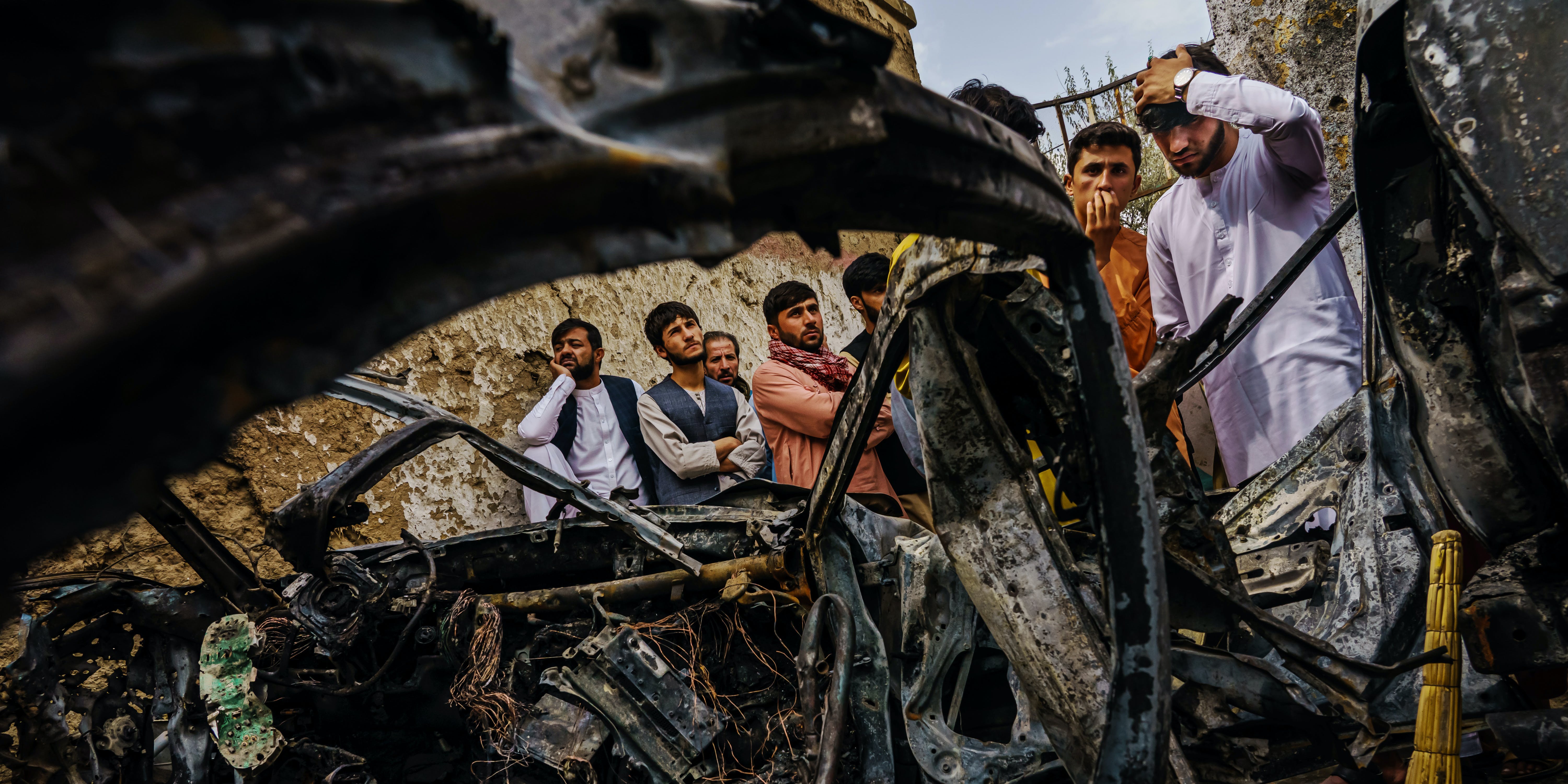 Relatives and neighbors of the Ahmadi family gather around the incinerated husk of a vehicle targeted and hit by an American drone strike, which killed 10 people including children, in Kabul on Aug. 30, 2021. 