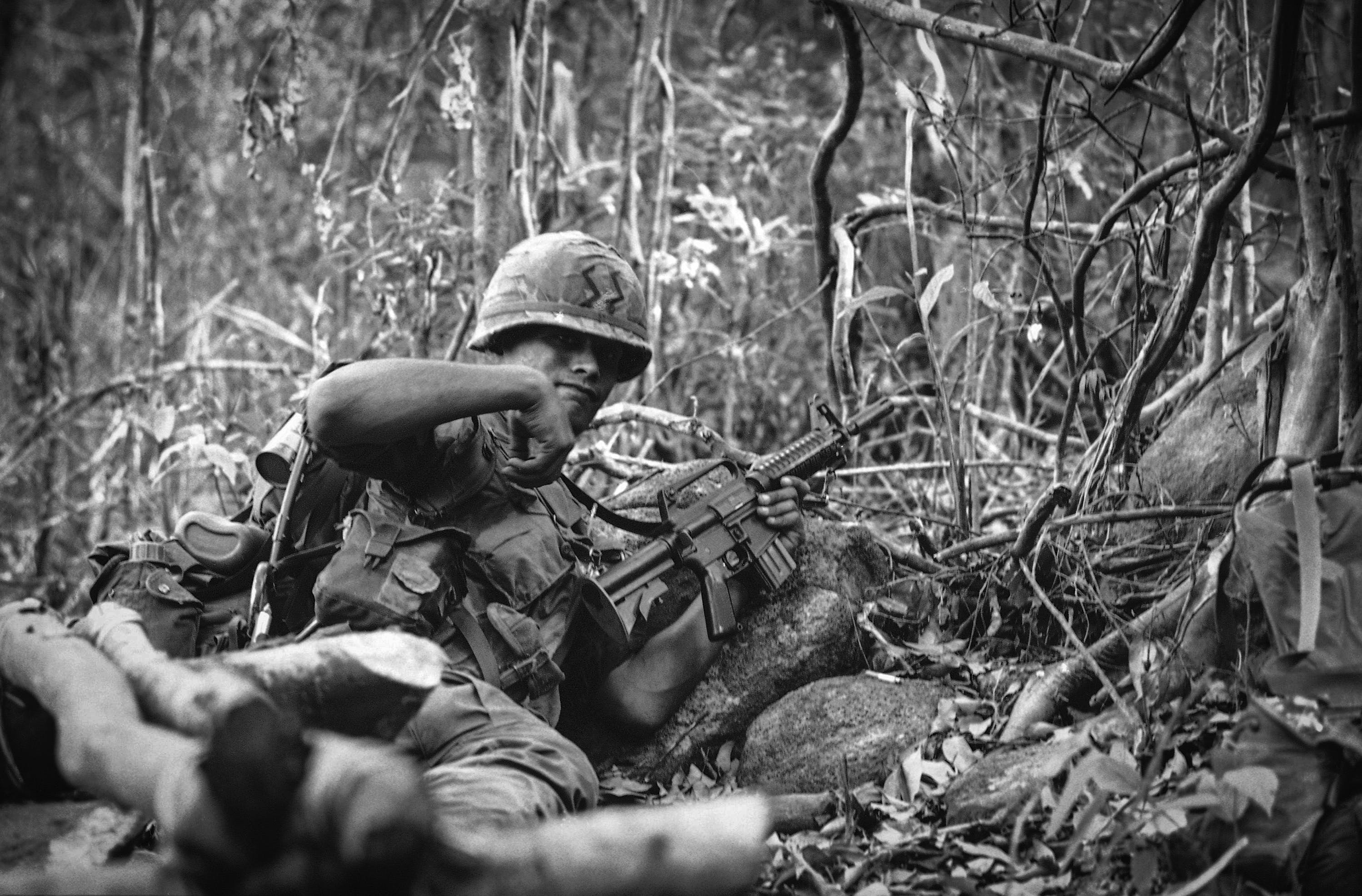 A paratrooper crouches behind rocks as he signals to members of his squad to form a defensive perimeter after it was hit while leading a patrol near Duc Pho, 330 miles northeast of Saigon on June 5, 1967. The patrol of the 327th regiment of the 101st airborne division took some casualties, but then drove off the enemy in a short-range rifle fight. Paratrooper holds the AR-15 -- a modified version of the M-16 automatic rifle. AR-15 has a collapsible stock, shorter barrel and a flash hider. (AP Photo)