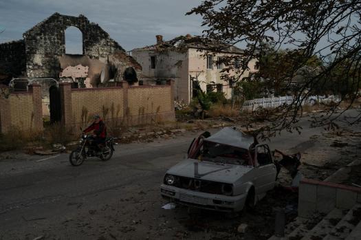 A man drives his motorcycle past a destroyed car in the retaken village of Velyka Oleksandrivka, Ukraine, Wednesday, Oct. 12, 2022. (AP Photo/Leo Correa)
