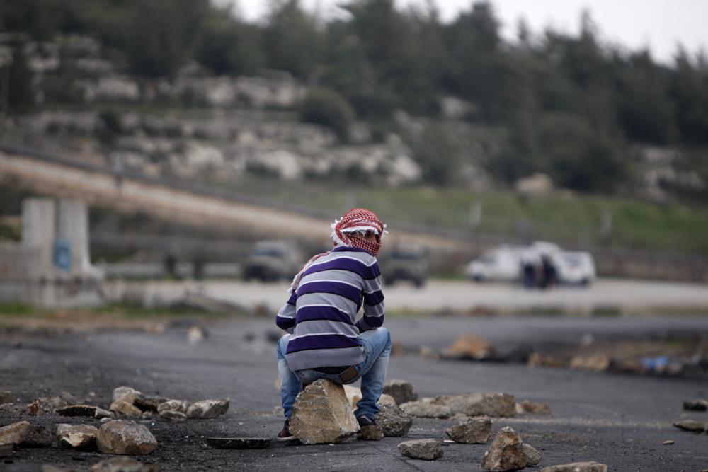 FILE - A masked Palestinian sits during a support rally for the Palestinian prisoners, outside Ofer, an Israeli military prison near the West Bank city of Ramallah, Friday, March 1, 2013. Israel's parliament on Wednesday overwhelmingly approved a law to strip Arabs convicted in nationalistic attacks of their Israeli citizenship or residency and deport them if they have accepted stipends from the Palestinian Authority. (AP Photo/Majdi Mohammed, File)