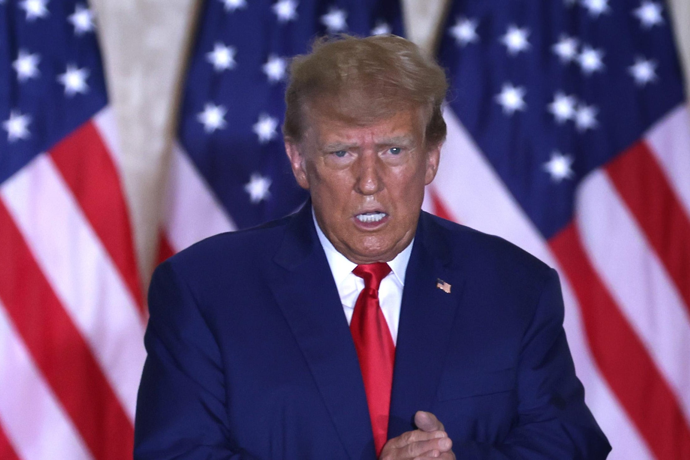 Trump clapping his hands slackjawed and jelly-eyed in front of a row of American flags.