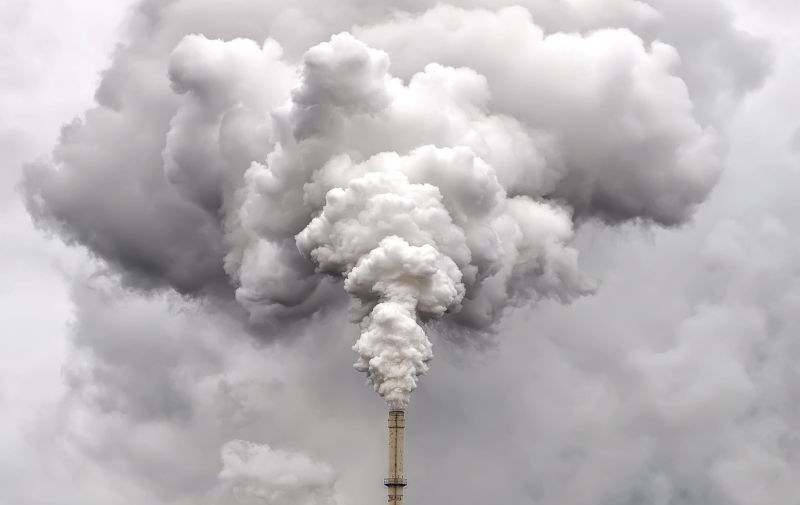 Smoke from factory pipe against dark overcast sky.
