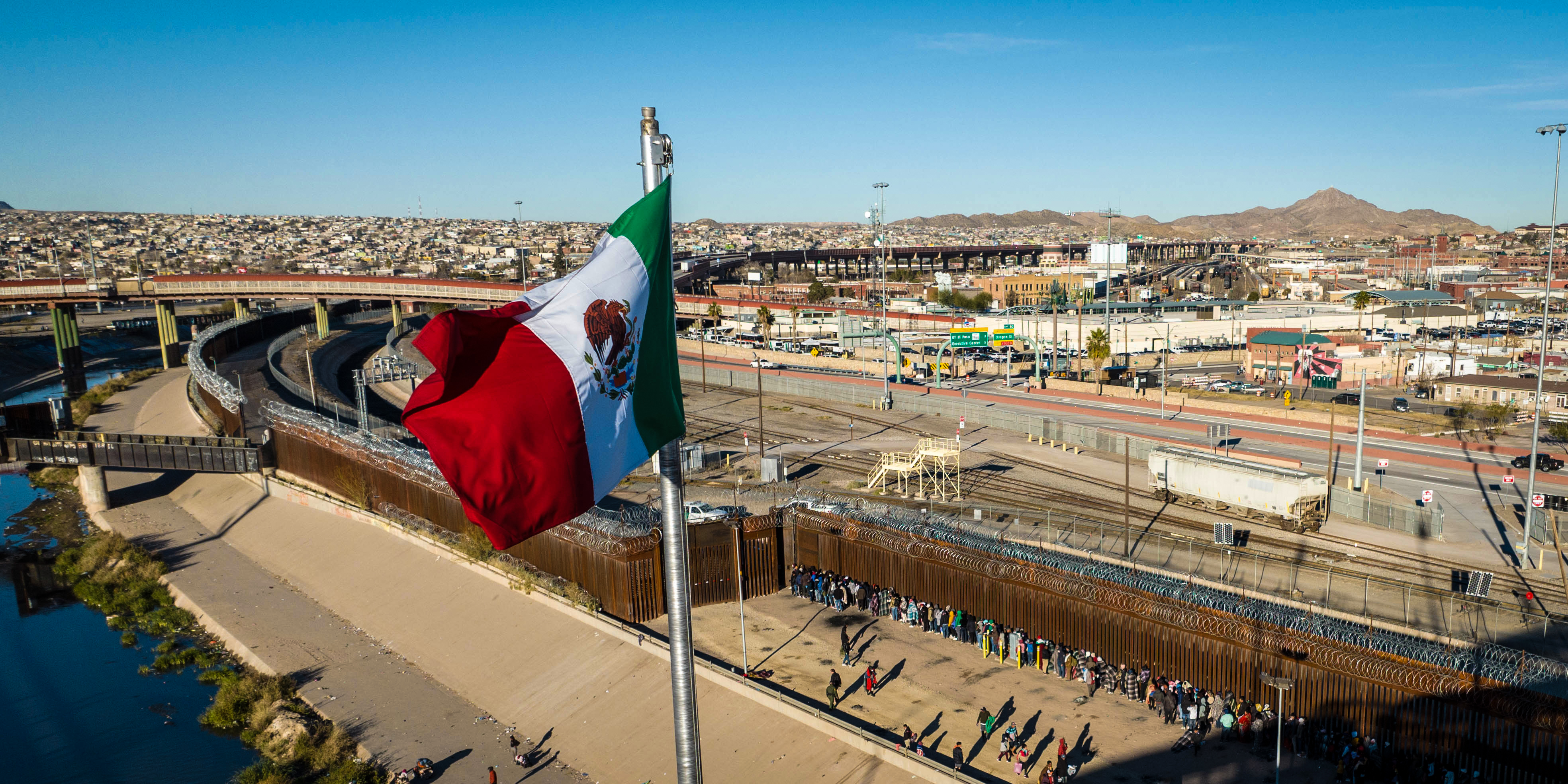 EL PASO, TEXAS - DECEMBER 22: An aerial view of the Mexican and American flags fly over an international bridge as immigrants line up next to the U.S.-Mexico border fence to seek asylum on December 22, 2022 in El Paso, Texas. A spike in the number of migrants seeking asylum in the United States has challenged local, state and federal authorities. The numbers are expected to increase as the fate of the Title 42 authority to expel migrants remains in limbo pending a Supreme Court decision expected after Christmas.  (Photo by John Moore/Getty Images)