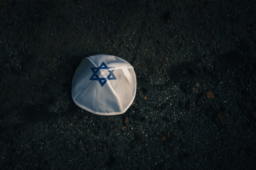 Knitted kippah cap in Israeli flag style on a dark asphalt road.