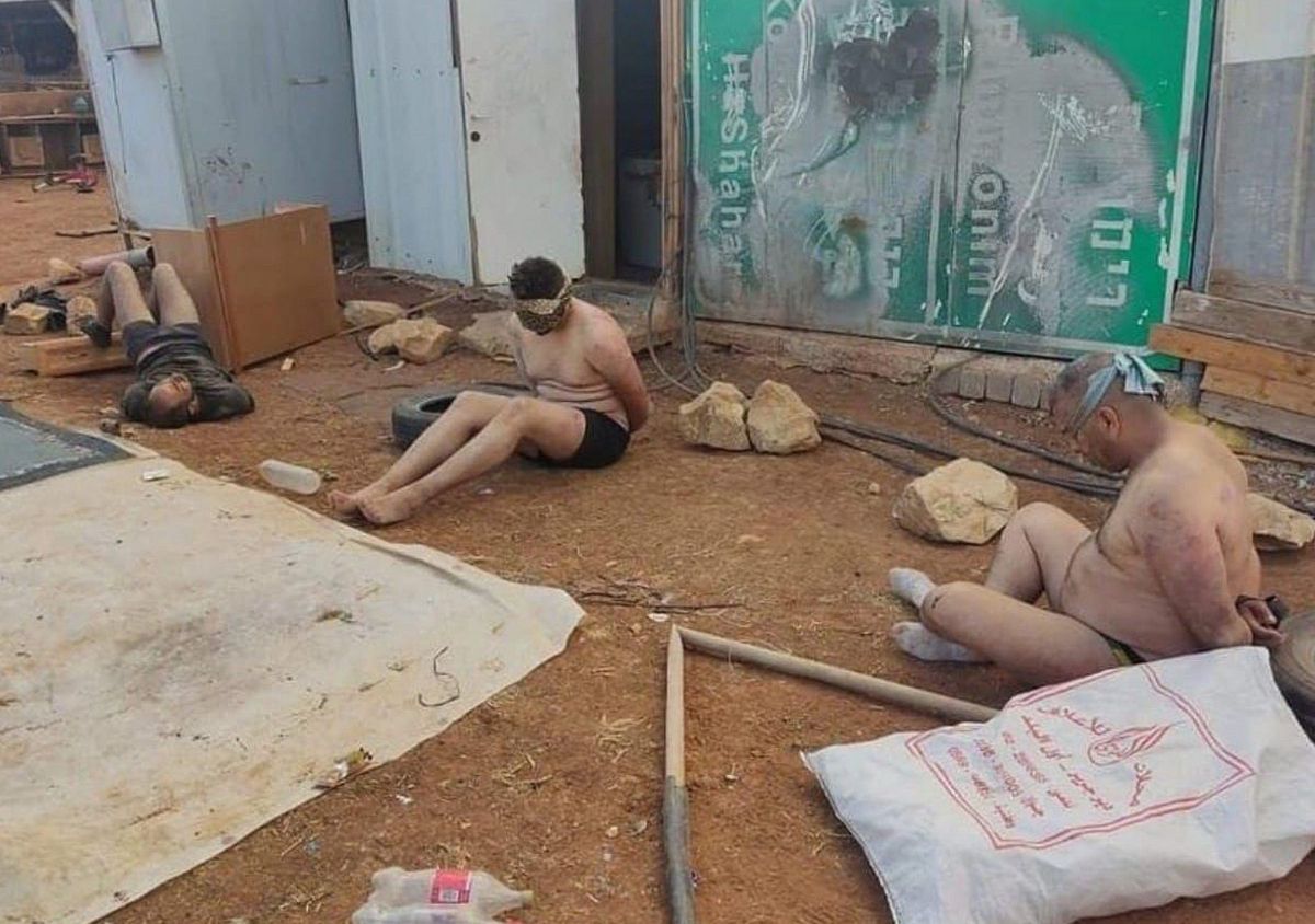 Stripped, blindfolded, and bound Palestinian men detained by Israeli forces sit on the ground 