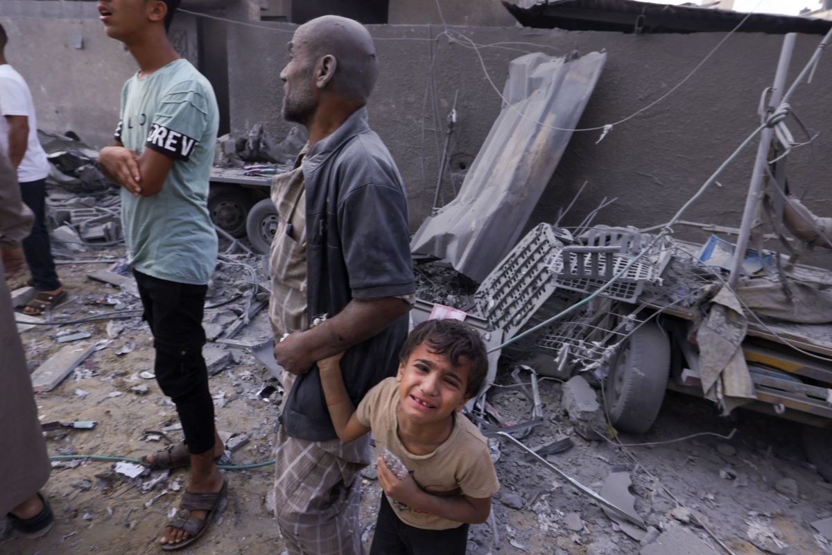 A Palestinian man covered in dust holds the hand of a weeping child