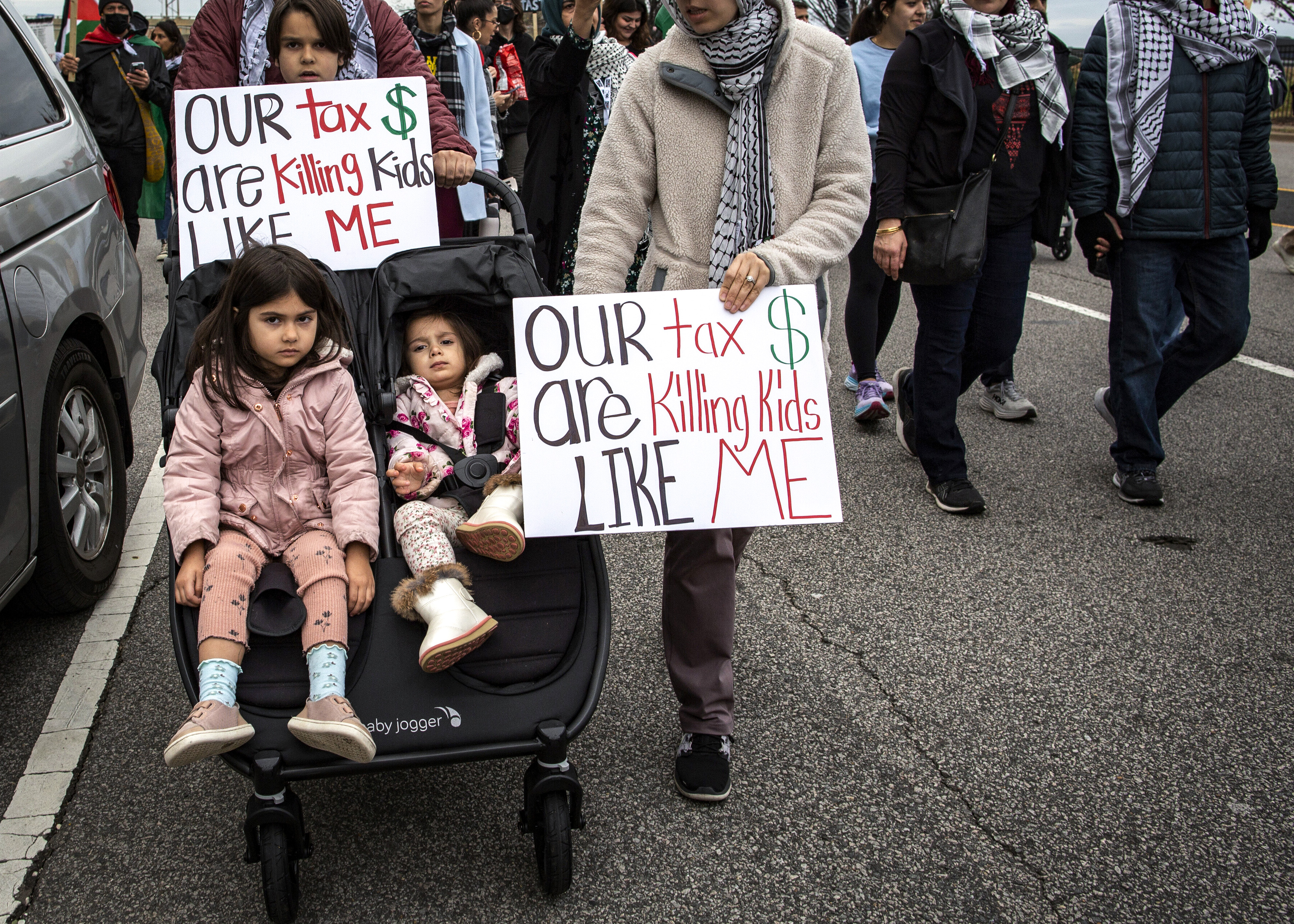 ARLINGTON, VA, UNITED STATES - 2023/12/09: Parents with their kids holding a sign with Our tax dollar are killing kids like me written on it as they join in a demonstration. Pro-Palestinian demonstrators gather at Pentagon City Metro in Arlington and then march to the City with Palestinian flags and banners, calling for a permanent ceasefire in Gaza. (Photo by Probal Rashid/LightRocket via Getty Images)