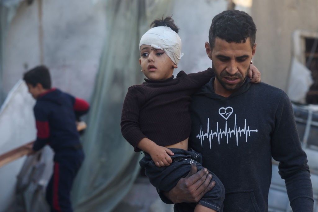 Palestinian boy with bandaged head held by a man in Gaza