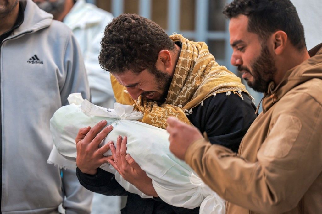 Palestinian man mourns child wrapped in cloth in Gaza on December 19, 2023