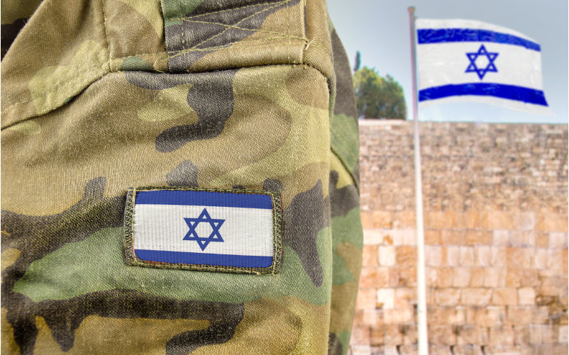 Military-man-posing-in-front-of-Israel-flag-and-The-Western-Wall. Image: iStock / Cunaplus_M.Faba Military man posing in front of Israel flag and The Western Wall background in Jerusalem