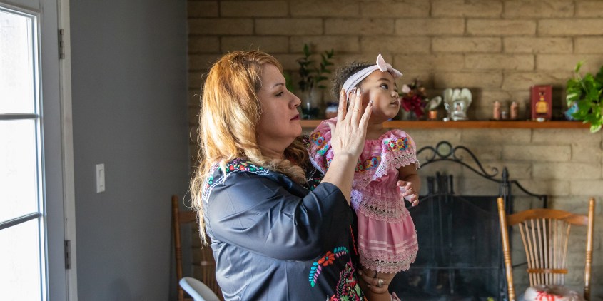 Martha Rodriguez comforts her 14-month-old granddaughter MD on October 20, 2023 at home in Phoenix, AZ. Childcare has become too expensive for her family so Rodriguez steps in after her early morning shift at an industrial laundry while her daughter works.