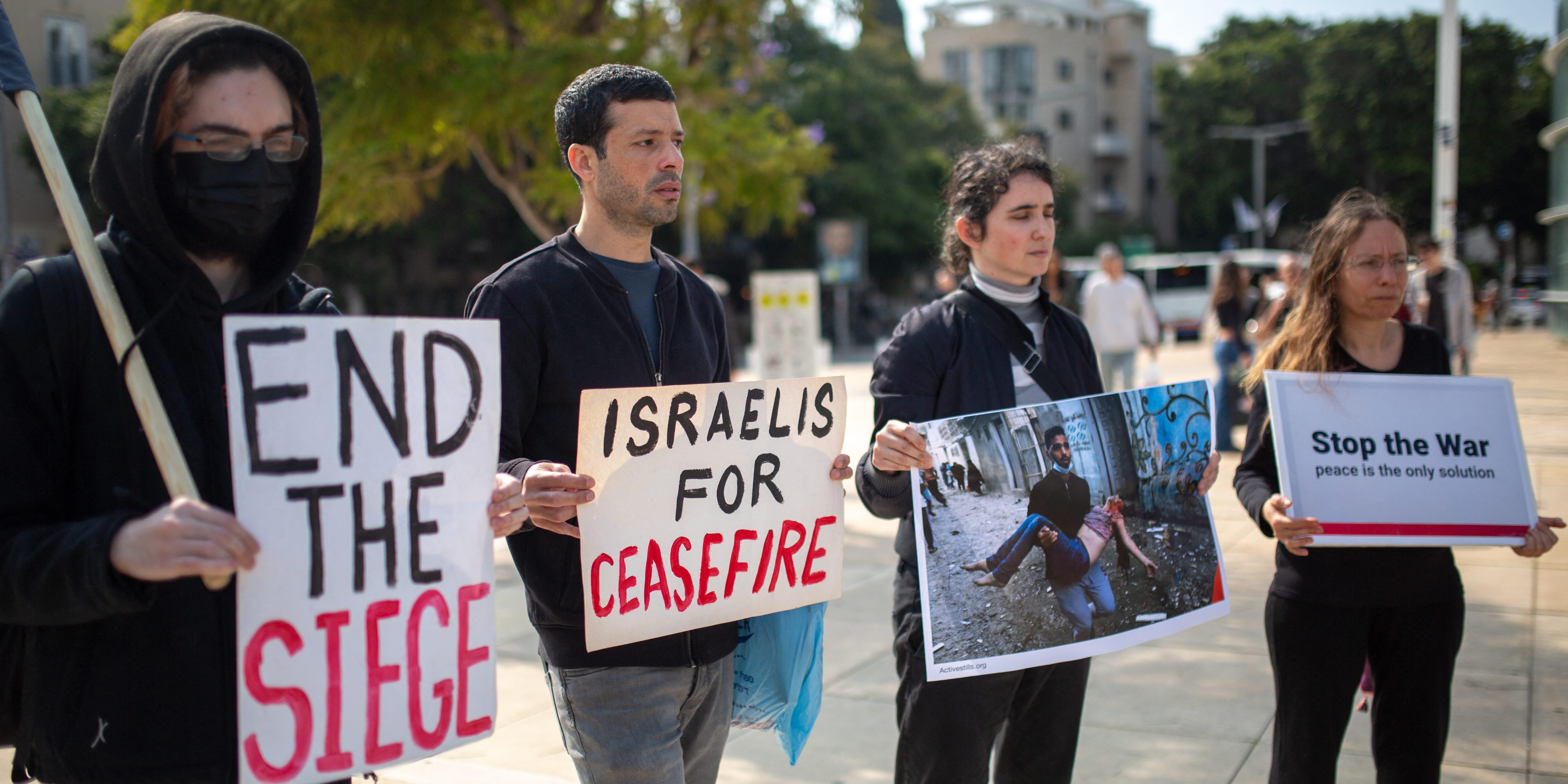 On municipal elections day, activists hold a series of signs at an anti-war protest in the center of Tel Aviv in Habima Square. The signs say "end the siege," "Israelis for Ceasefire" and "Stop the War; Peace is the Only Solution," and one sign shows an image of a Gazan man holding a bloody child after an Israeli airstrike. (Photo by Emily Glick / Middle East Images / Middle East Images via AFP) (Photo by EMILY GLICK/Middle East Images/AFP via Getty Images)