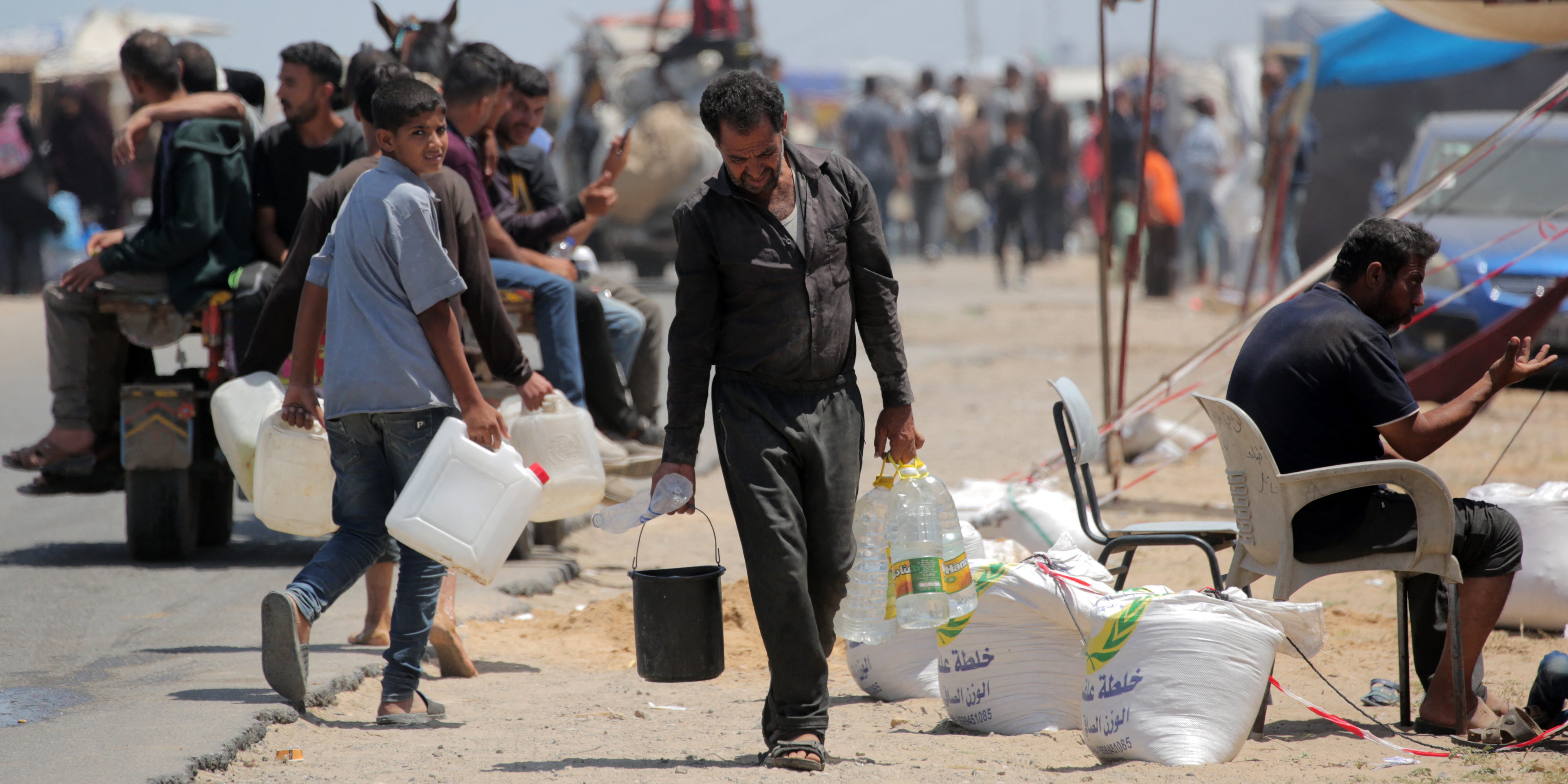 Palestinians who sought refuge in Deir el-Balah after fleeing Rafah in the southern Gaza Strip, carry water to their tents at a makeshift camp on May 12, 2024, amid the ongoing conflict between Israel and the Hamas militant group. (Photo by AFP) (Photo by -/AFP via Getty Images)