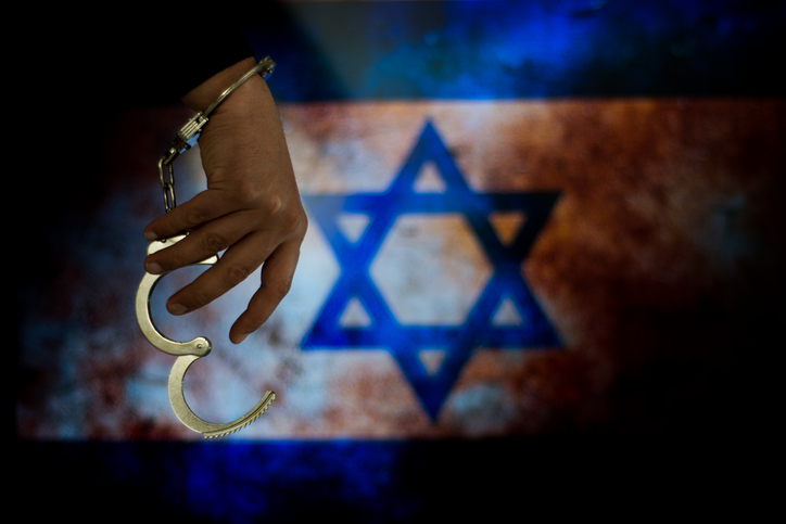Handcuffs with hand in front of flag. Image: iStock/ilkaydede