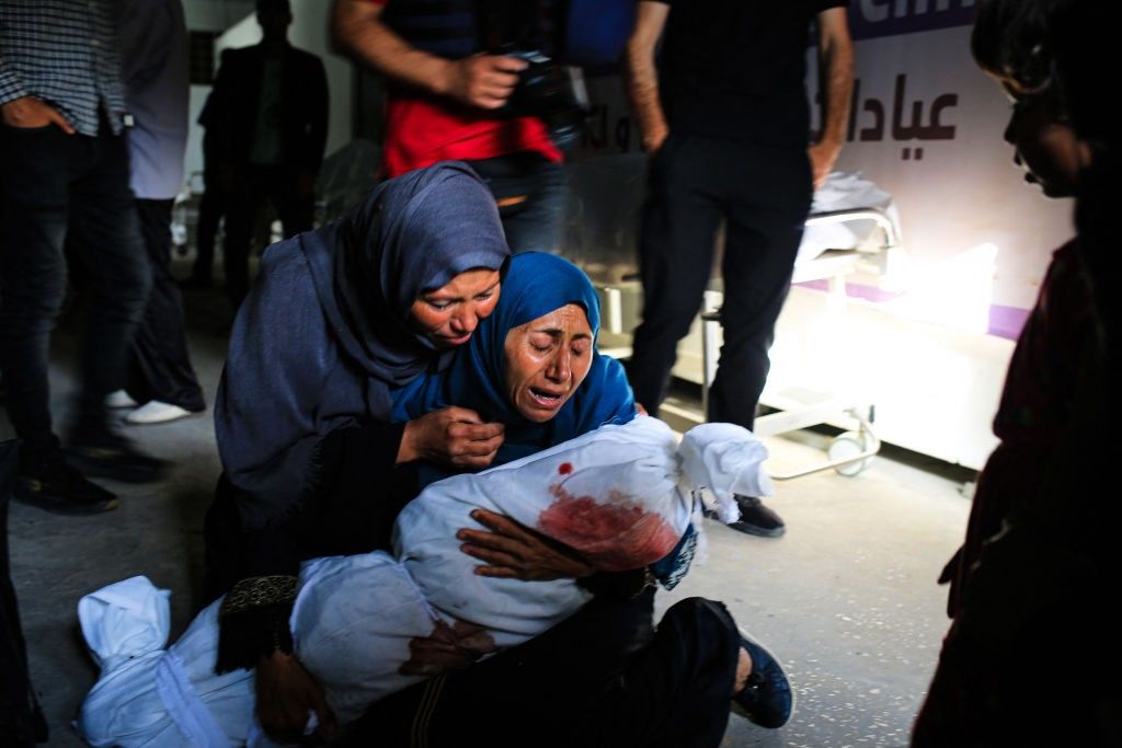 Palestinian women weep as one holds the shrouded body of a child killed by an Israeli strike